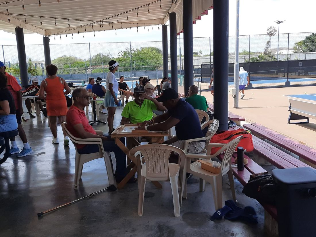 Leden onder de patio, domino aan tafel en tennis op de achtergrond